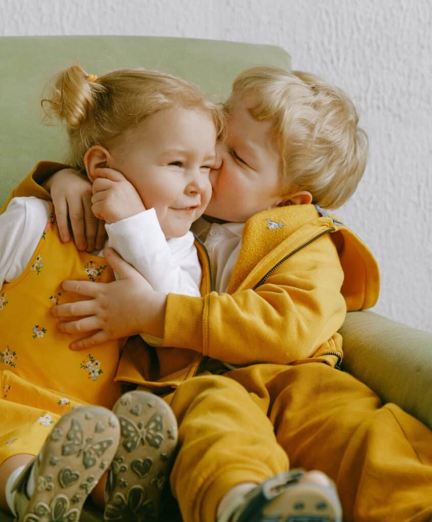 Toddler Boy Hugging Toddler Girl And Kissing Her On The Cheek. 