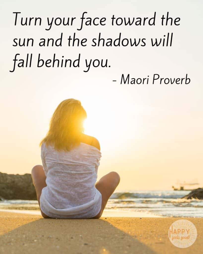 Turn Your Face Toward The Sun And The Shadows Will Fall Behind You. A Woman Is Sitting On The Beach Facing The Sun And Her Shadow Is Behind Her.