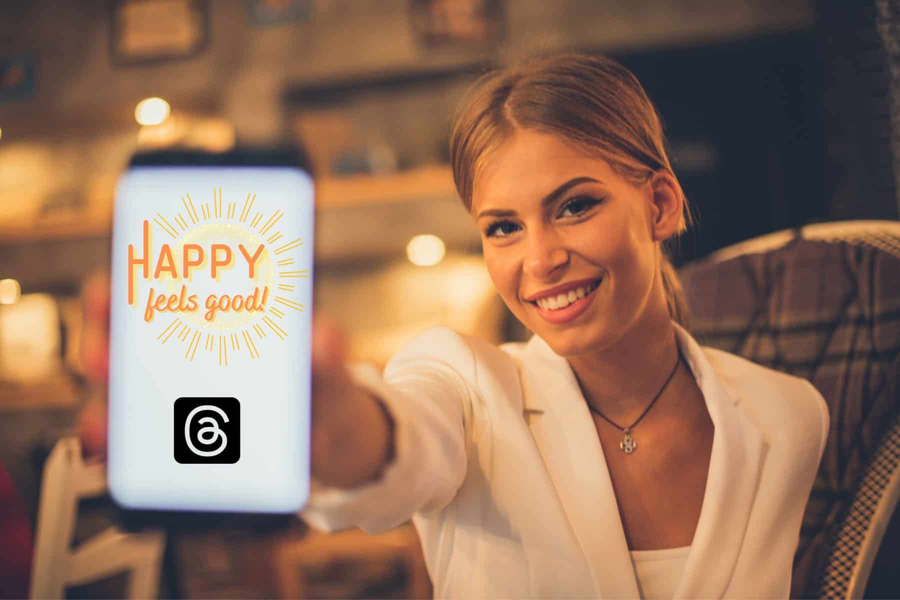 Smiling Young Woman Holding Phone Out. Screen Shows Happy Feels Good Is Tied Up With Threads Logo.
